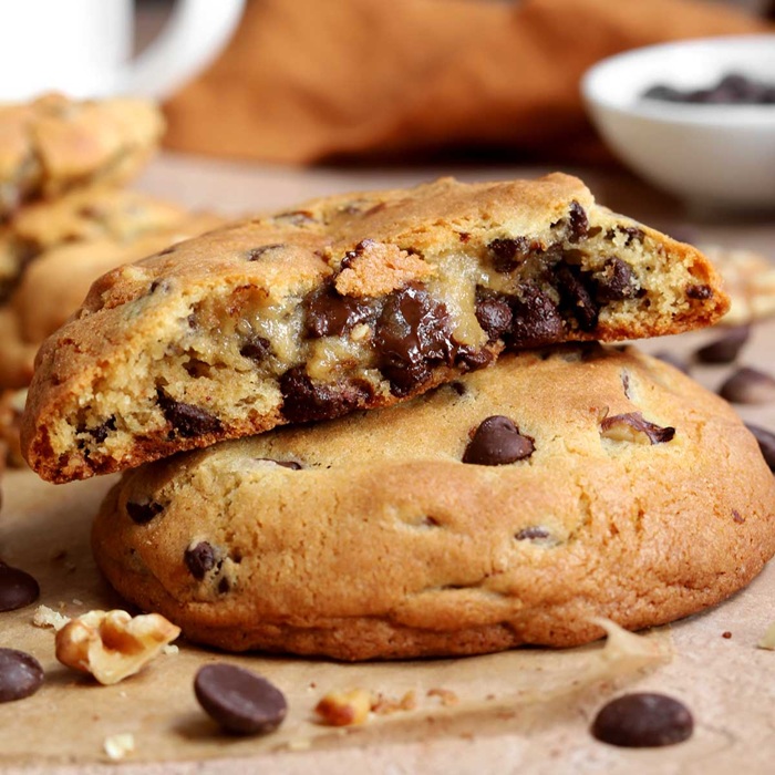 Two chocolate chip cookies stacked on top of each other. The top cookie has a bite taken out of it.