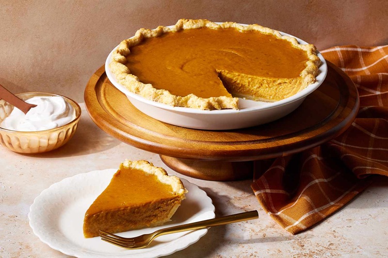 A picture of a pumpkin pie with a slice cut out of it next to a bowl of frosting.