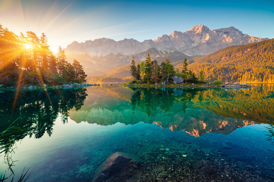 A photograph of a beautiful scenic lake with the sun shining in the left-hand corner.